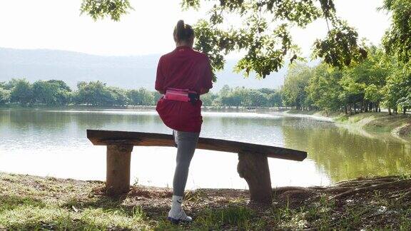 早晨一位亚洲妇女在公园池塘边的长凳上暖脚