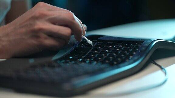特写镜头:一位不知名的男子坐在桌边用棉签清理从按钮上拆卸下来的脏黑键盘