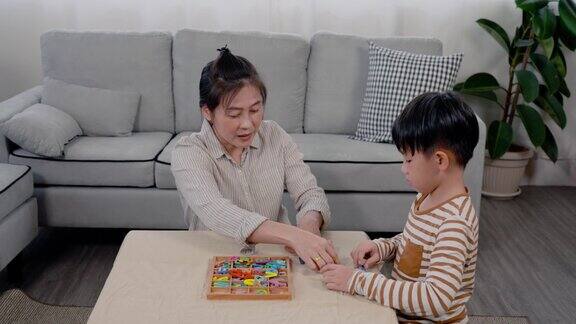 4K亚洲单身妈妈和他英俊的儿子他们在一起度过空闲时间做活动妈妈和儿子在客厅的木桌上玩单词板玩得很开心