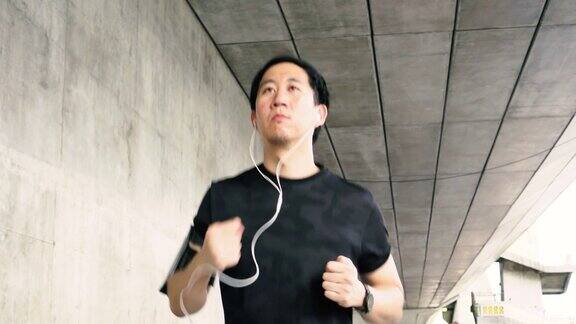 一个年轻的亚洲人戴着耳机在城市里跑步