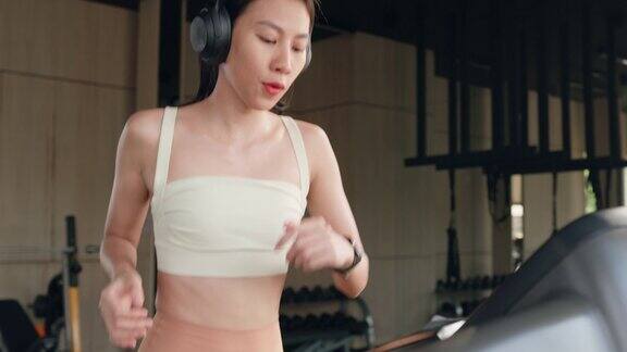 年轻的亚洲运动女性戴上无线耳机用智能手机打开播客音乐播放列表在跑步机上跑步在现代化的健身房积极训练运动人士锻炼