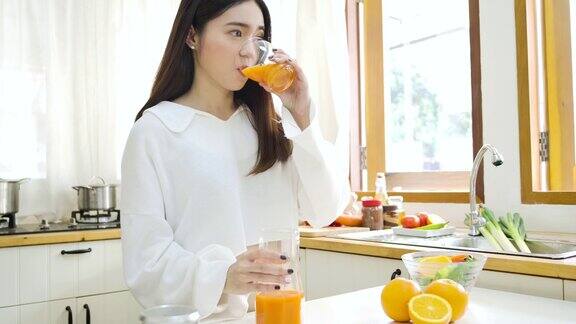 快乐的亚洲女人在厨房喝橙汁健康的饮食和健康