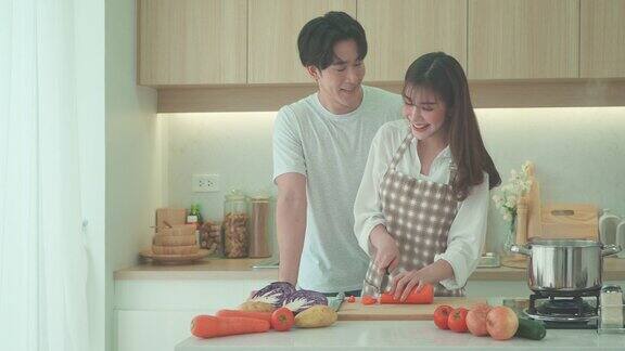 一对亚洲夫妇正在家里的厨房里帮忙切胡萝卜做鸡汤一对情侣的浪漫场景