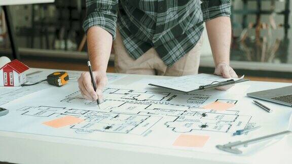 室内设计师或建筑师审查蓝图和拿着铅笔画在书桌上在家里的办公室