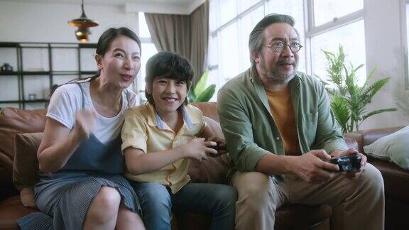 家庭时光亚洲父母和儿子一起坐在家中客厅的沙发沙发上放松地玩游戏机开怀大笑开心微笑亚洲家庭homs隔离隔离的理念