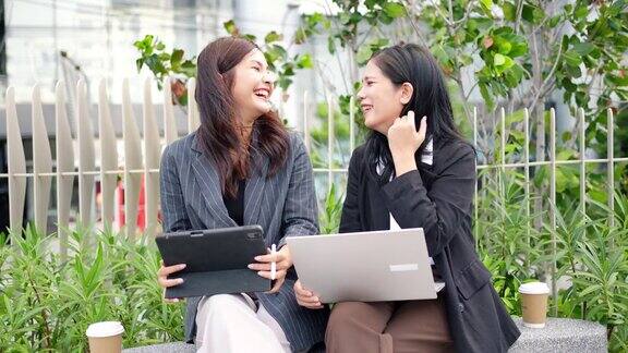 在办公室外使用笔记本电脑工作的商务人士两个年轻的亚洲女商务人士正在开会和同事一起讨论