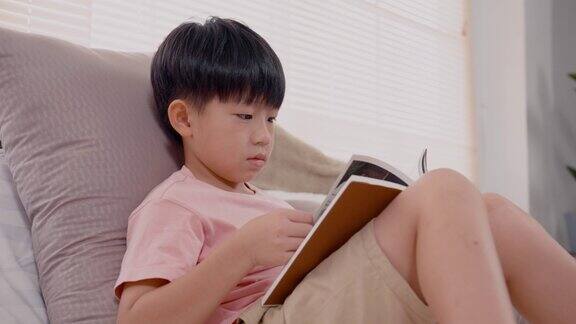 4K9岁的亚洲男孩坐着看书他很高兴每天在他的床上在房子的卧室里他很快地复习他所学到的东西