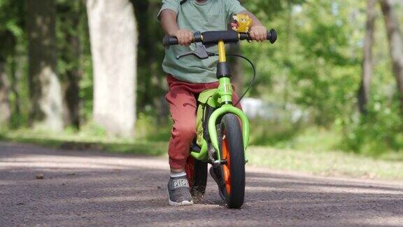 蹒跚学步的孩子戴着保护头盔在夏季公园骑平衡自行车