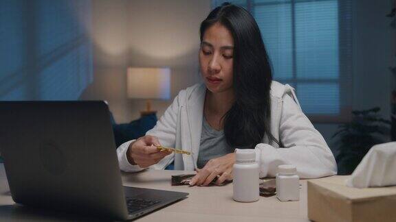 生病的年轻亚洲妇女使用笔记本电脑在家里的客厅晚上与医生交谈