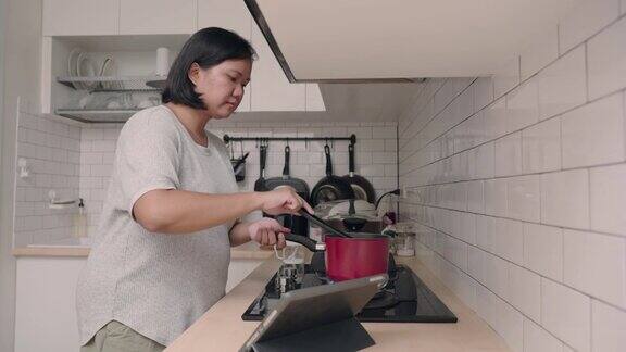 亚洲妇女在厨房做饭同时看平板电脑的食谱