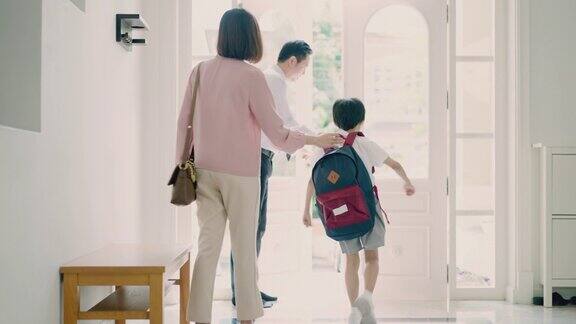 亚洲父亲在早上上学前给儿子系鞋带可爱的小男孩背着双肩包在妈妈的帮助下幸福的家庭亚裔父母和他们的儿子走出前门他的孩子第一天上学