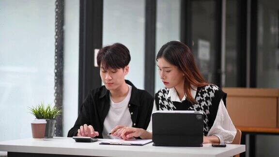 两名亚洲商务人士在办公室用智能手机和笔记本电脑交谈