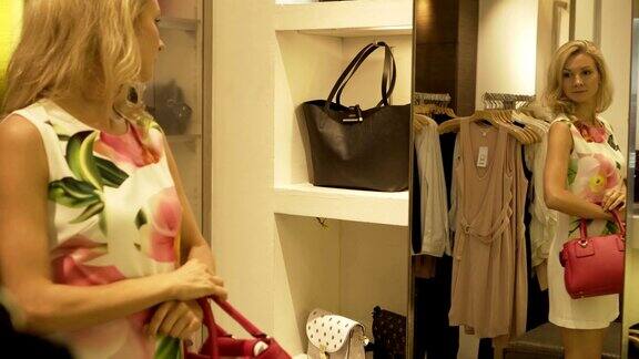金发女郎站在服装店的镜子旁试穿手提包