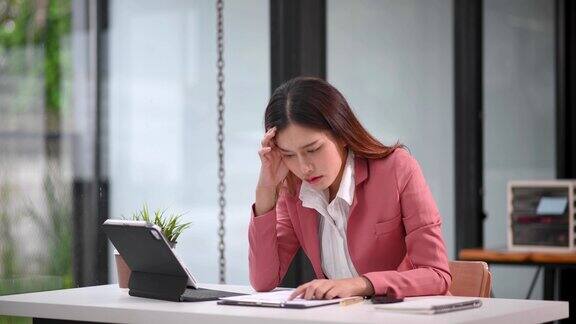 亚洲女性感到头痛在现代办公室里用笔记本电脑和平板电脑工作时过度劳累的女商人金融家