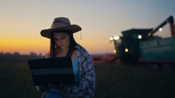 蓝色时间女农艺师在联合收割机前用笔记本电脑将玉米卸到拖车上