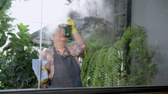 亚洲老年妇女身体健康系上围裙携带喷雾瓶清洗玻璃的布在玻璃上喷清洁剂为了不划伤玻璃早上开业前要清洁咖啡店外