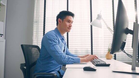 亚洲英俊的商人使用笔记本电脑在办公室工作有魅力的专业男性员工坐在桌子上感到快乐享受在公司工作场所的休闲时间