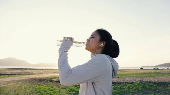 年轻的亚洲女人跑步喝水后在户外的山