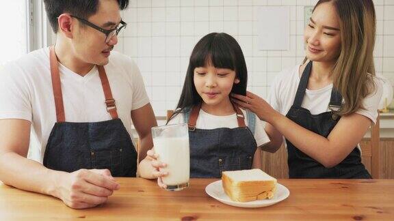 亚洲家庭在舒适的厨房享受早餐小女孩女儿坐在桌子上喝牛奶微笑在早上幸福的家庭在客厅