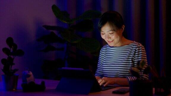 亚洲妇女晚上在家里办公室用笔记本电脑在键盘上打字