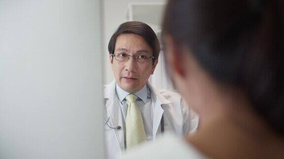 中年男医生在医院办公室会诊时向女病人解释的镜头