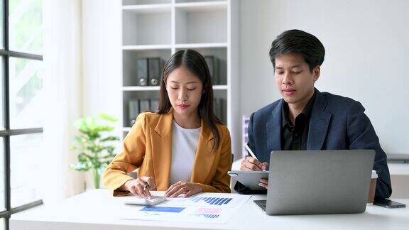 两名亚洲商务人士在办公室用智能手机和笔记本电脑交谈
