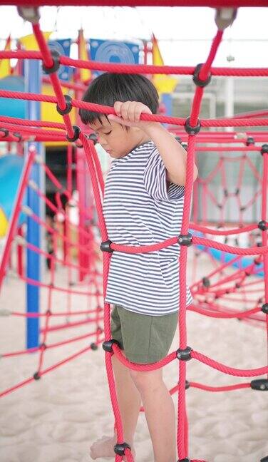 一个小男孩正在操场上的绳网上爬