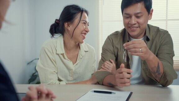 女销售员保持房子的钥匙年轻的亚洲夫妇与休闲坐在桌子上感觉幸福的新房屋合同协议在房地产办公室