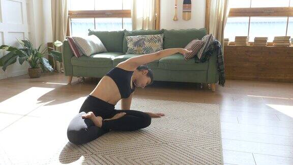 年轻的印度女子冥想坐在地毯上做伸展运动做瑜伽黑色运动服灯光房间在家里的早晨