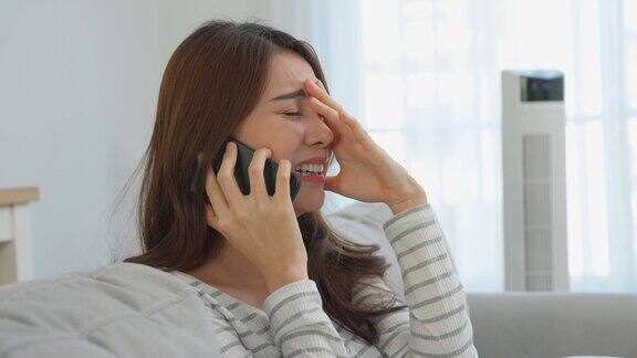 亚洲美女坐在沙发上在家里打电话有吸引力的年轻女孩感到悲伤和哭泣而讨论在智能手机与朋友的生活问题和心碎在客厅