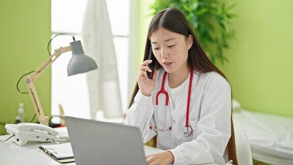 年轻的中国女医生在诊所用笔记本电脑和智能手机通话