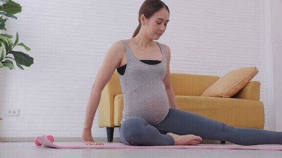 年轻漂亮的亚洲孕妇穿着运动服在家里做瑜伽