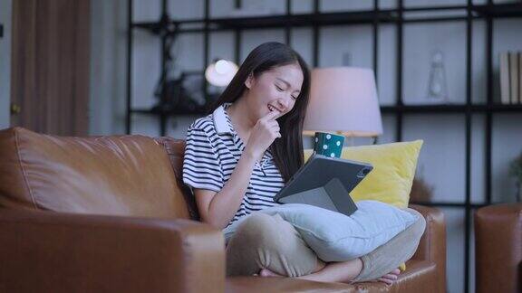 年轻迷人的亚洲女性在家里工作手用平板电脑检查业务数据图表计划报告休闲放松在沙发上在客厅居家隔离