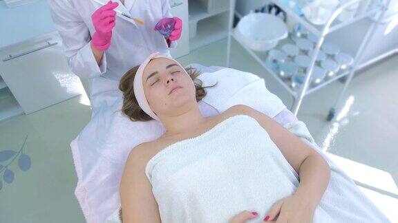 美容师在诊所用刷子在女性脸上涂抹脱皮乳液