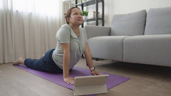 瑜伽眼镜蛇姿势年轻的亚洲女性在客厅用数码平板电脑做瑜伽练习