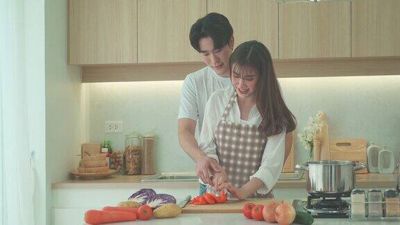 一对亚洲夫妇正在家里的厨房里帮忙切胡萝卜做鸡汤一对情侣的浪漫场景