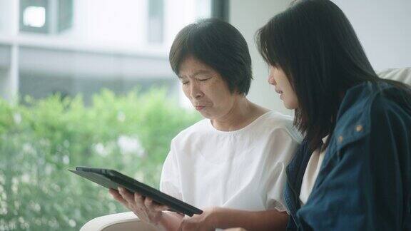 老年妇女和女儿在客厅学习使用数码平板电脑