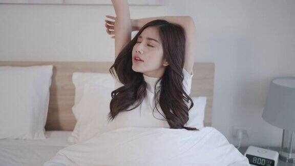 美丽的亚洲女人躺在白色的床上拿着黑色的闹钟震惊地学习在家里的卧室早上晚些时候