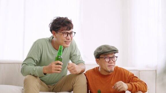 4K亚洲男子朋友一起在家里看电视上的体育比赛