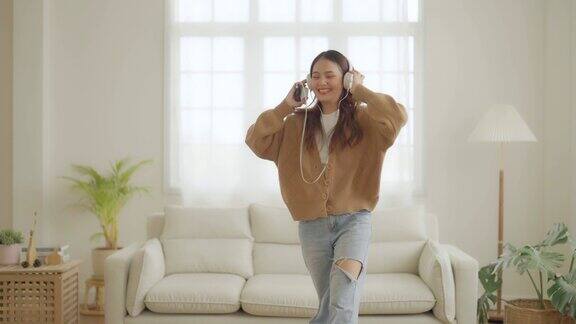 年轻的亚洲女性戴着耳机在家里客厅的地板上跳舞