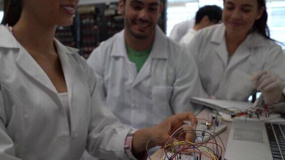 美丽的女学生解释她的实验室伙伴如何连接在电子实验室工作