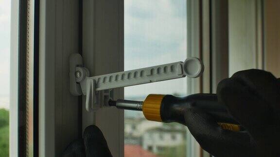 公用螺丝刀拧紧塑料开窗限位器固定螺钉带手套的手特写用螺丝刀拧紧窗限位器固定螺钉到塑料窗框上回家修理