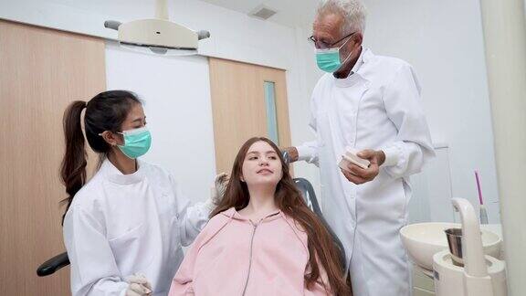 亚洲中年妇女牙科助理协助老牙医为坐在牙科椅上的十几岁女孩做牙科检查老牙医向她展示如何正确地进行牙科护理