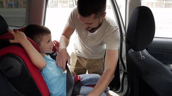 微笑的儿子在婴儿汽车座椅被放在后座的关怀父亲