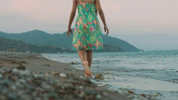日落时分一个年轻女孩在海滩上散步穿着衣服的女孩走在海边