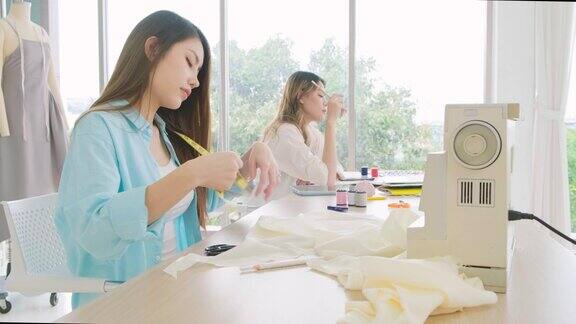 两个亚洲女裁缝或时装设计师用剪刀剪纸制作衣服的图案时装设计师在车间里为新系列的服装做裁缝或裁缝