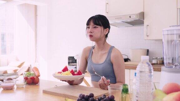 一位穿着运动服的亚洲女性在厨房里享用美味又营养的水果小吃她拥抱健康的生活方式在食用有益健康的食物中找到快乐
