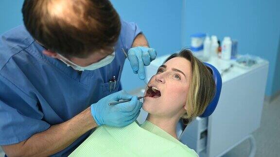 牙科医生在牙科诊所用牙科设备印模匙检查病人的牙齿口腔保健理念医生戴着一次性医用口罩微笑着快乐的女人