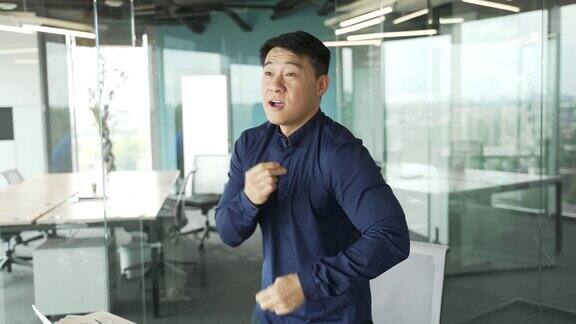 快乐的精力充沛的亚洲商人IT程序员庆祝成功在灯光玻璃办公室在室内慢动作跳舞
