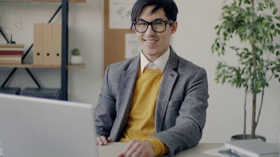 慢动作的肖像愉快的亚洲企业家坐在电脑桌前微笑在办公室